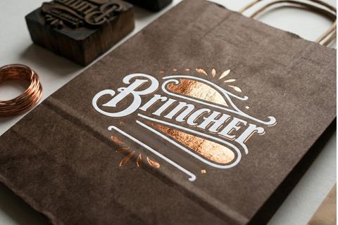 Kỹ thuật in mực trắng và ép kim nổi bật trên nền giấy sẫm màu của dịch vụ in túi giấy kraft.