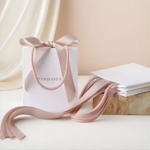 Mẫu túi giấy dây ruy băng cao cấp bằng giấy Ivory ép kim logo sang trọng thắt nơ lụa mềm mại.